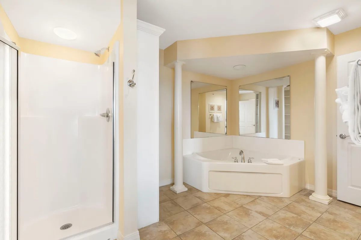 A luxurious ensuite bathroom featuring a soaker tub and separate shower stall, adorned with elegant columns and expansive mirrors. The setting is both spacious and serene, offering a spa-like environment for unwinding after a day on the lake.