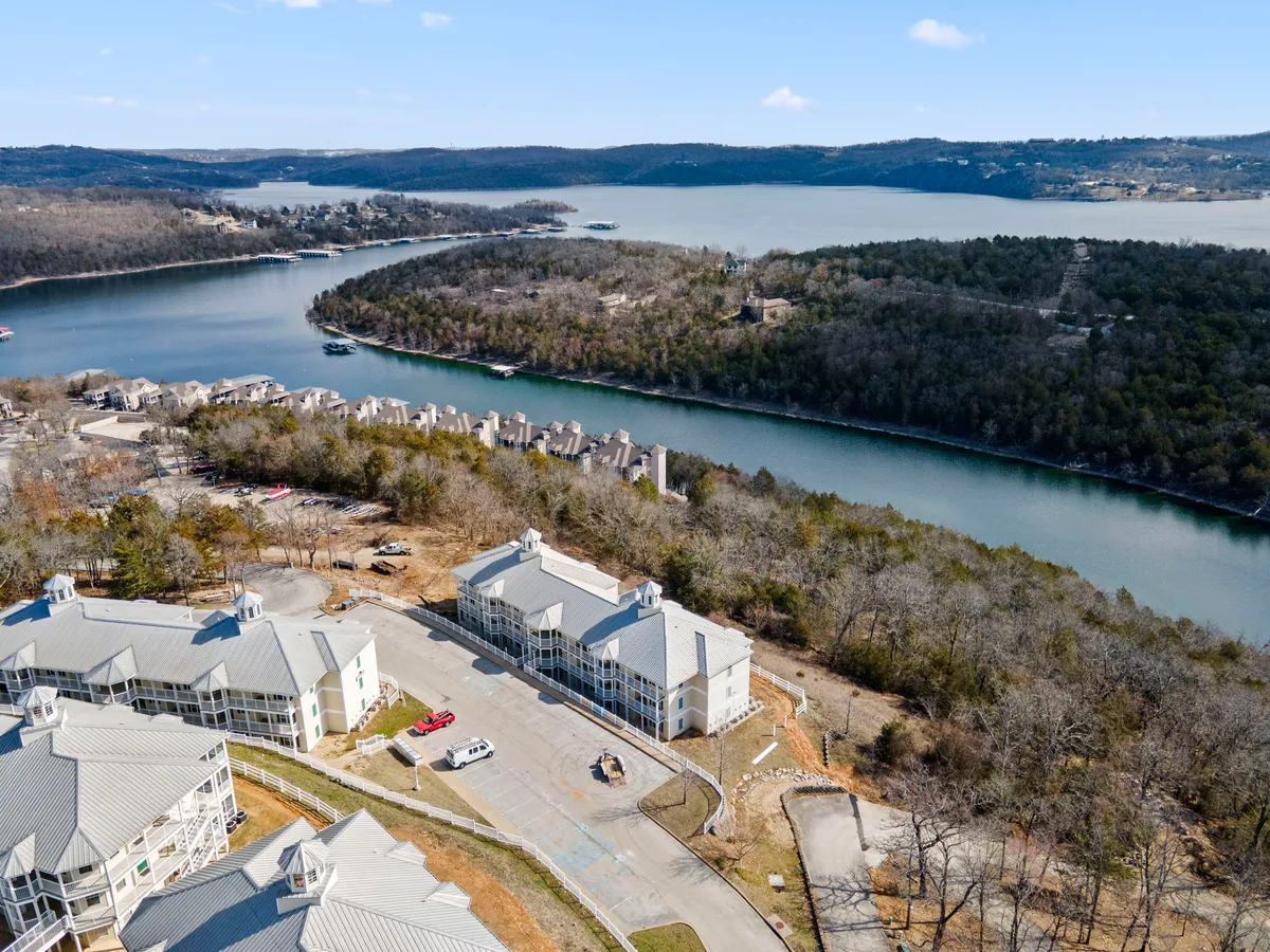 A serene exterior view featuring the sparkling lake bordered by surrounding hills and nearby buildings. There are clear paths along the lakeshore, inviting guests (and their pets) for nature walks or leisurely strolls. The sense of calm and open space suits the section's focus on pet-friendly outdoor relaxation.