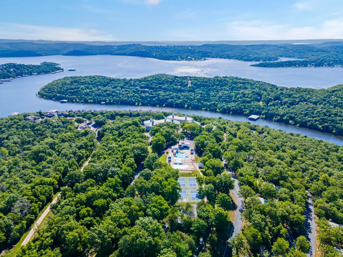A breathtaking elevated view encompassing expansive water scenes, lush greenery, a swimming pool, and tennis courts—all set within a secluded property. This image captures the natural beauty and recreational opportunities available near Ozark Vista 145, suggesting both lakeside serenity and active adventure.