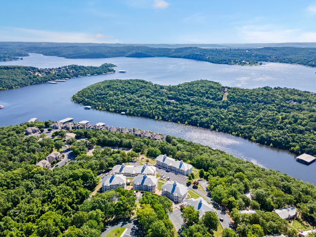 A tranquil exterior scene highlighting a waterfront area surrounded by lush forests and residential buildings. The image captures people engaging in activities like boating, hiking, and relaxing by the water, with the sun setting in the background. The natural landscape and lakeside setting evoke a sense of peacefulness and openness, perfect for outdoor adventures with pets.