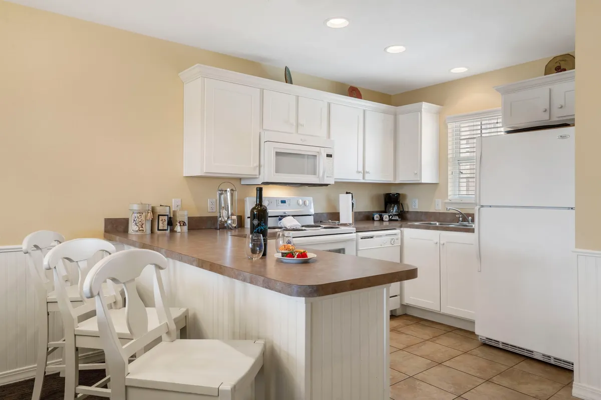 A welcoming kitchen with a spacious countertop, stools for casual seating, modern appliances, and bottles on display, suggesting a space primed for cooking and gathering.