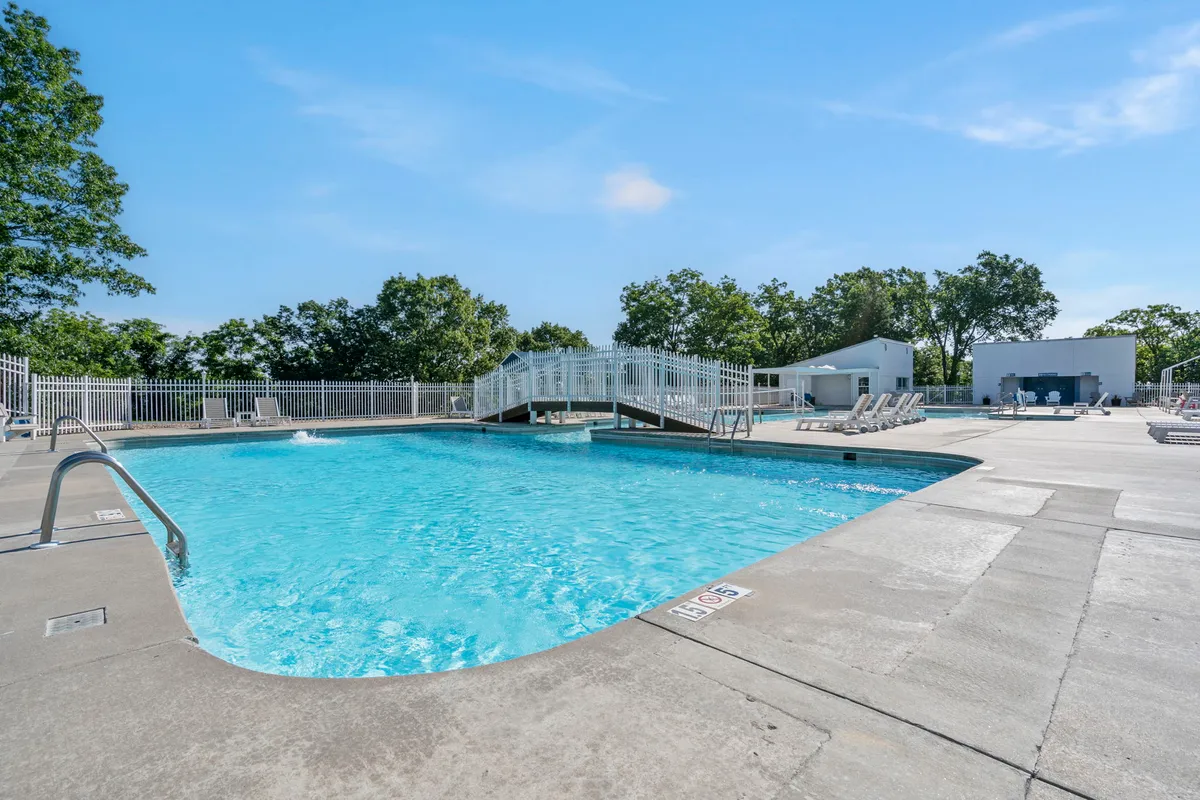 This image highlights the community's sparkling outdoor pool, complete with a picturesque bridge, inviting lounge chairs, and an overall leisurely and refreshing atmosphere. The pool is bathed in natural light and set against lush surroundings, evoking the quintessential summer experience for guests.