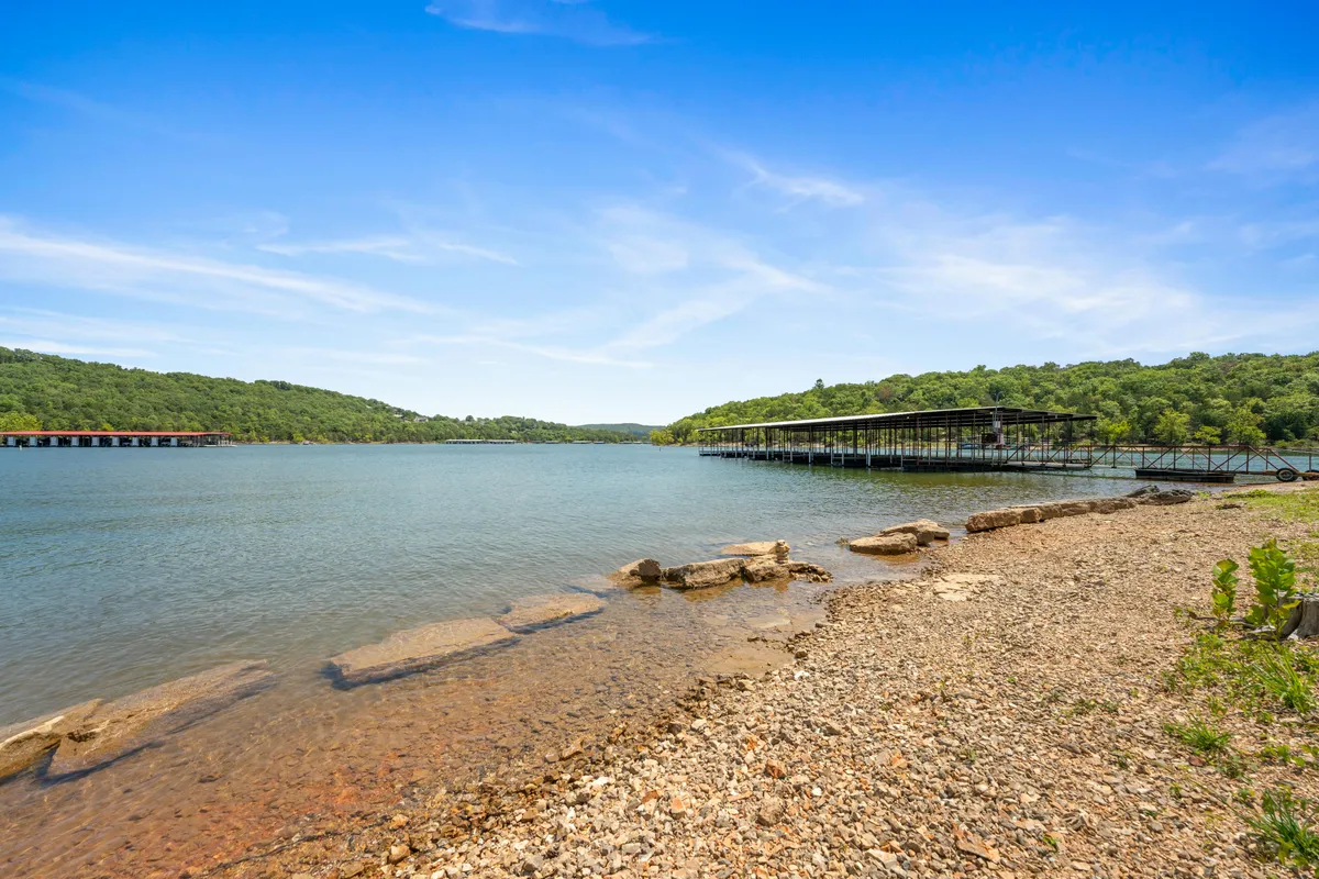 A peaceful lakeside scene with calm water, distant green hills, and dock structures extending into the lake. The setting is quiet and inviting, ideal for fishing, boating, and enjoying the natural beauty of Table Rock Lake.