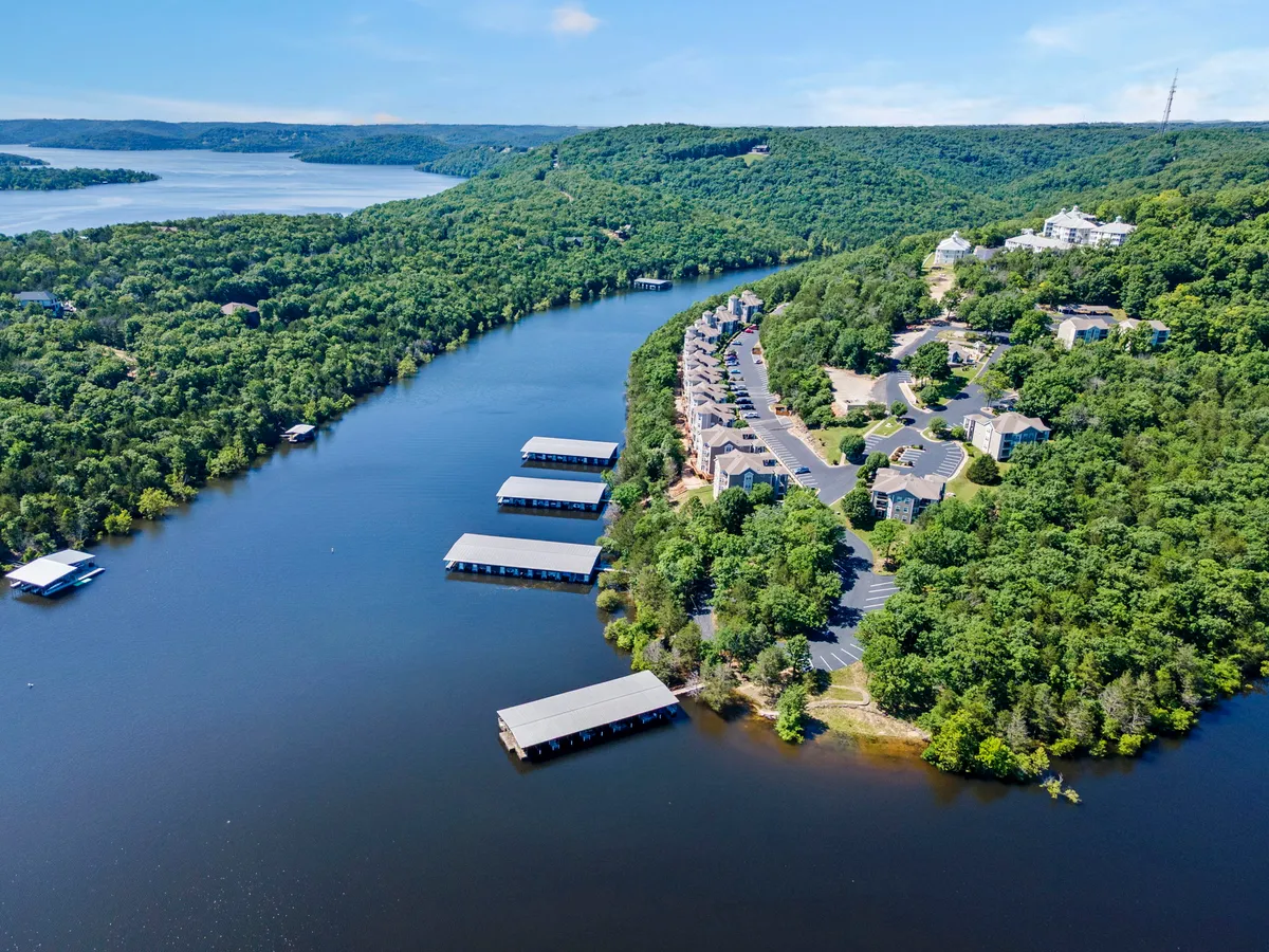 A sweeping exterior view of the lake with marinas, surrounding hills, and residential resort buildings. The peaceful water and lush greenery convey a tranquil, rejuvenating resort setting, ideal for walks or unwinding by the shore.