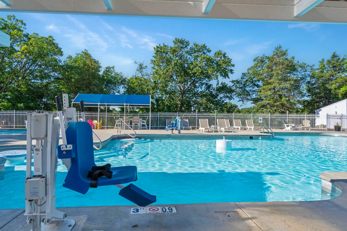 A sparkling outdoor pool surrounded by lush trees, lounge chairs, and a shaded canopy. The pool area is alive with guests swimming, relaxing, and socializing, capturing the active, communal resort lifestyle.