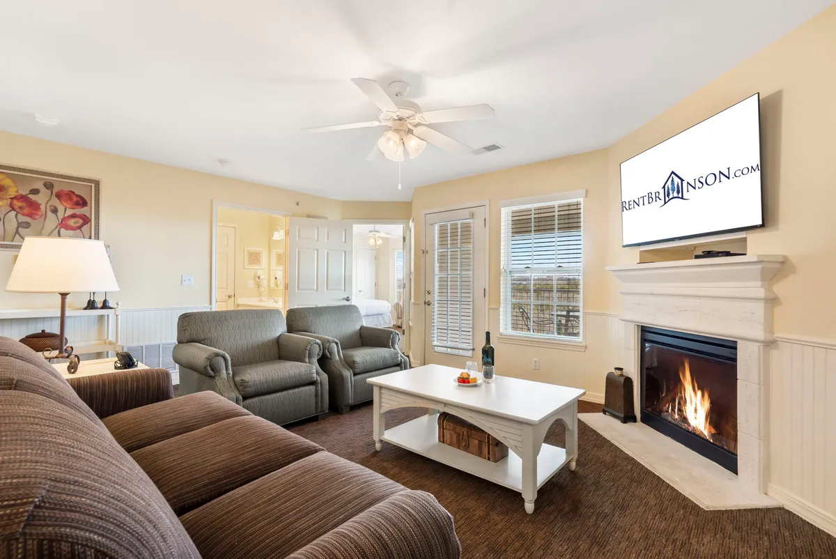 The image showcases a warm, inviting living area with a glowing fireplace at its center, plush seating arranged for conversation, a coffee table, and a large TV—creating a perfect space for relaxation and bonding after a day by the lake.