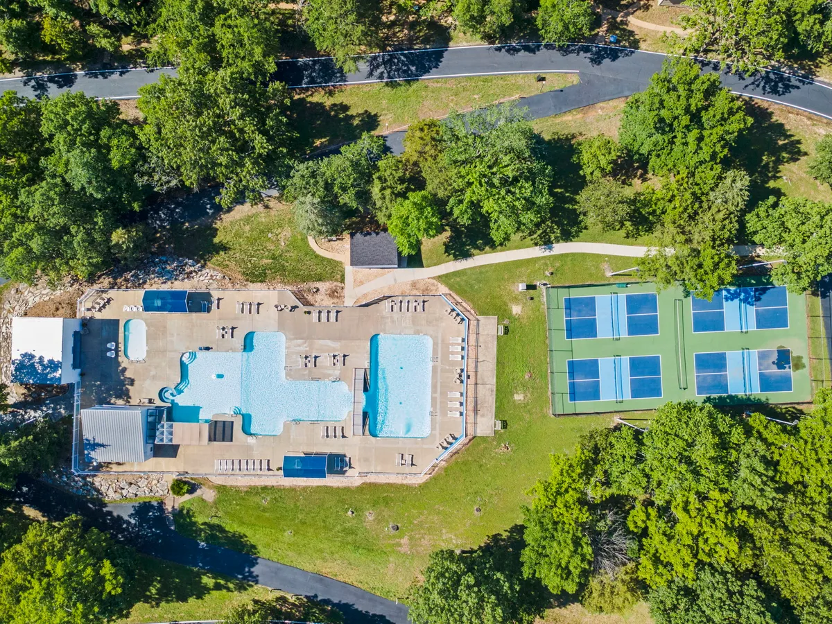 A large outdoor swimming pool sits at the center, surrounded by tennis courts, lounge chairs, and verdant landscaping. The area is abuzz with the energy of recreational activities, offering options for swimming, tennis, and social gatherings.