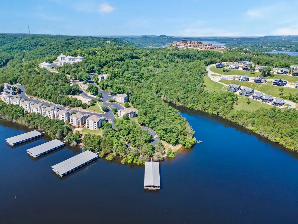 A tranquil lakeside setting with docks stretching over the water, residential buildings nestled in greenery, and open space for boating, fishing, or simply relaxing by the lake.